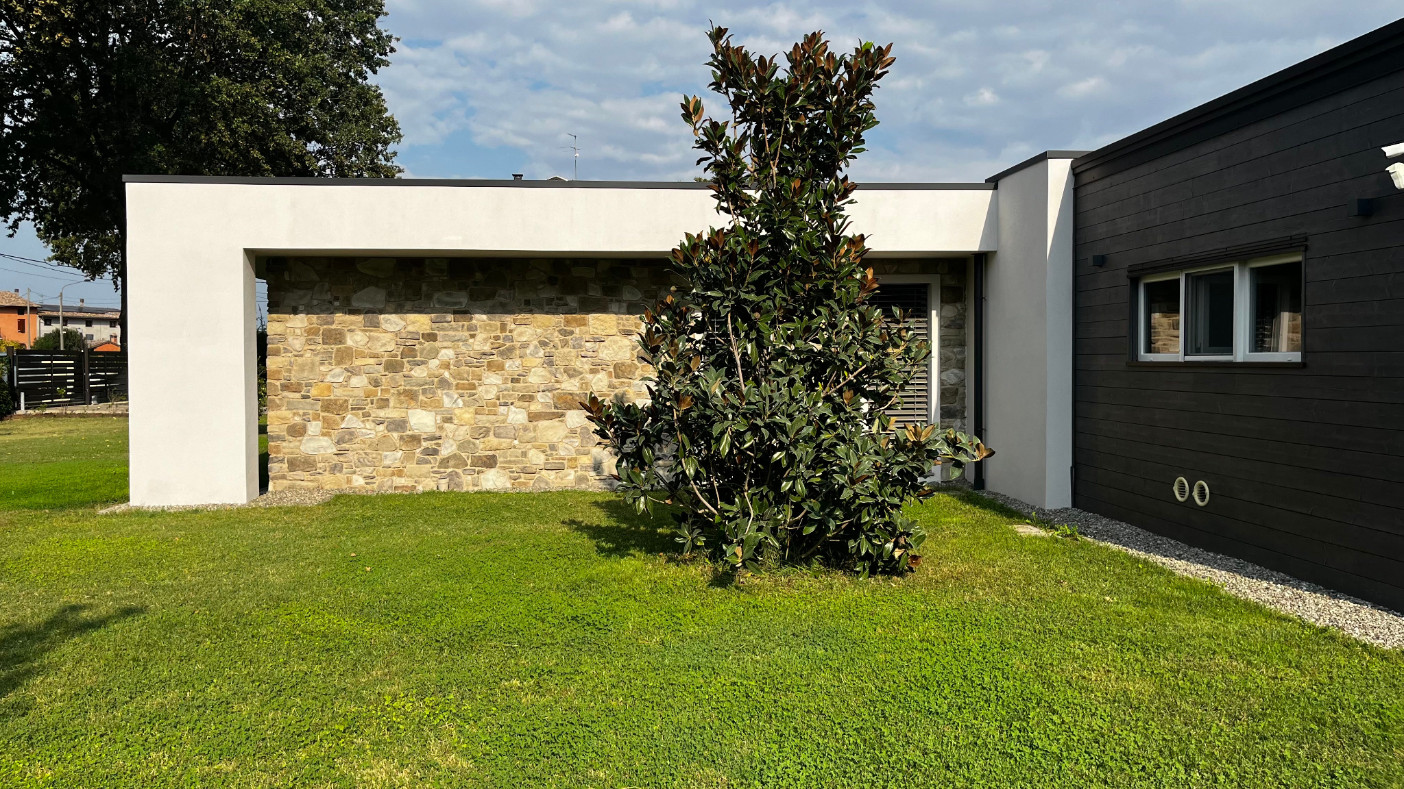 Villa A|M, volume bianco, parete in pietra, albero centrale e volume scuro