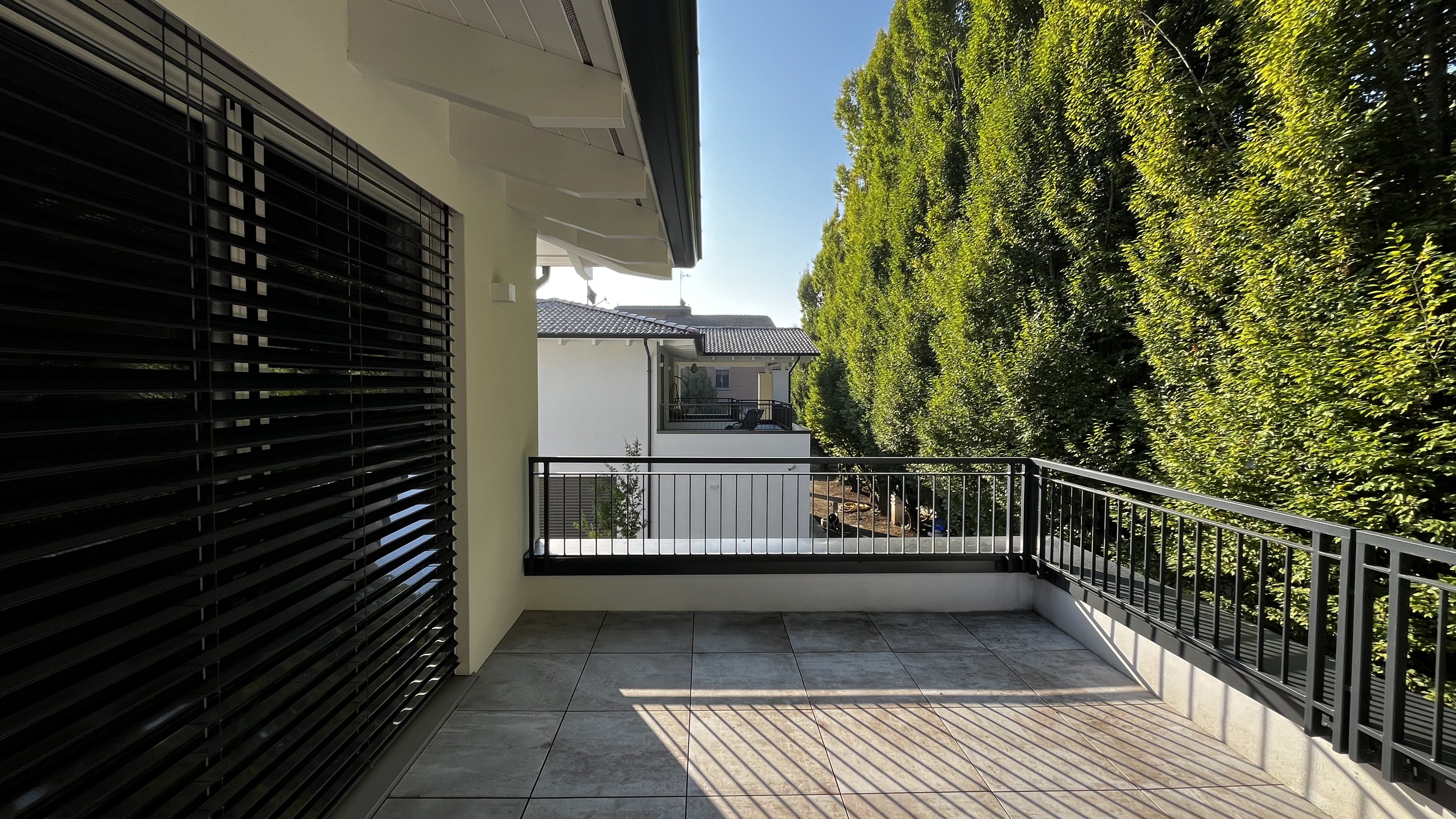 Terrazza al primo piano con vista sulla facciata specchiata della casa gemella, separata da una siepe alta