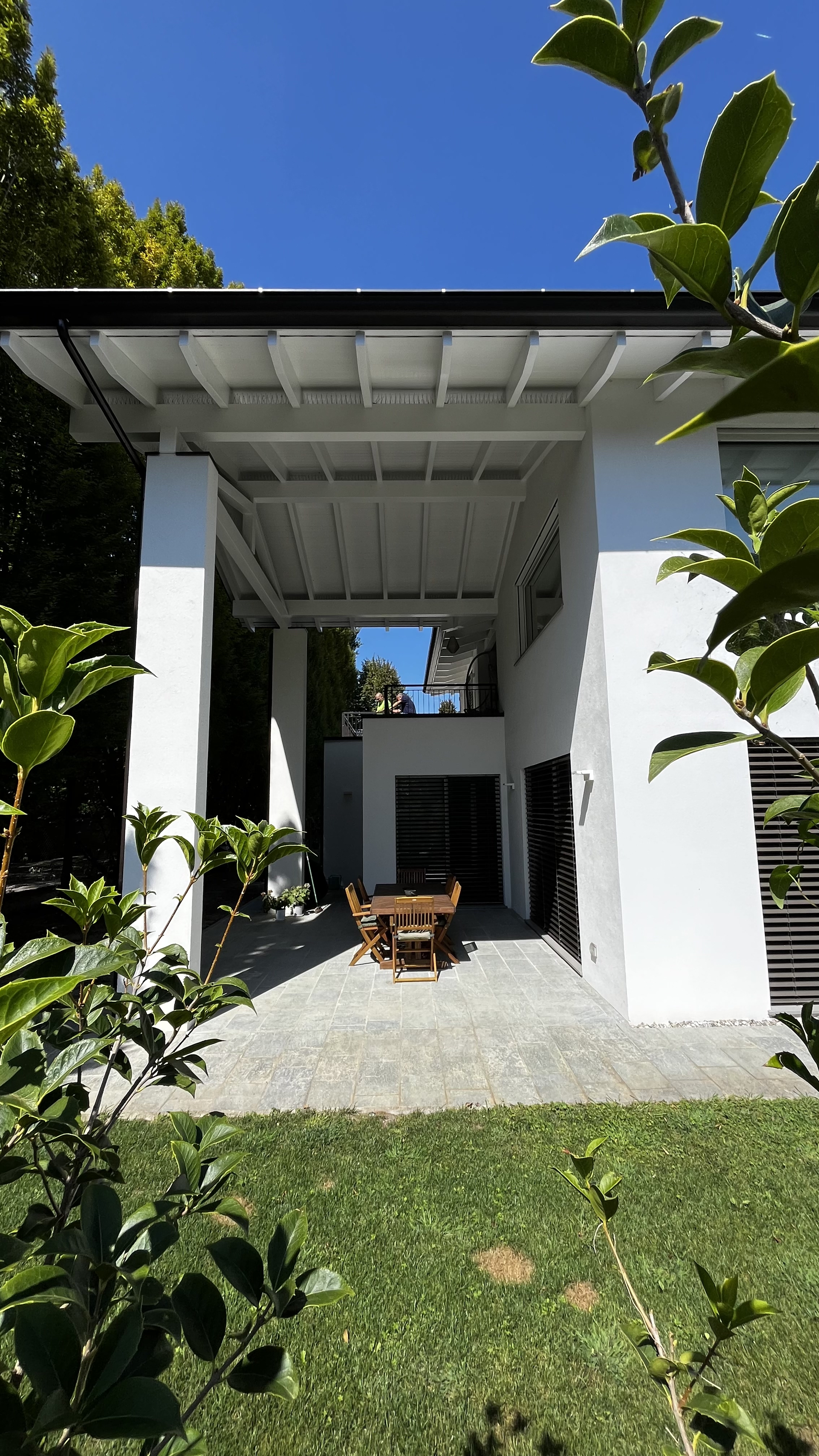 Patio coperto da un ampio porticato in legno, con tavolo da pranzo esterno e vista sul giardino